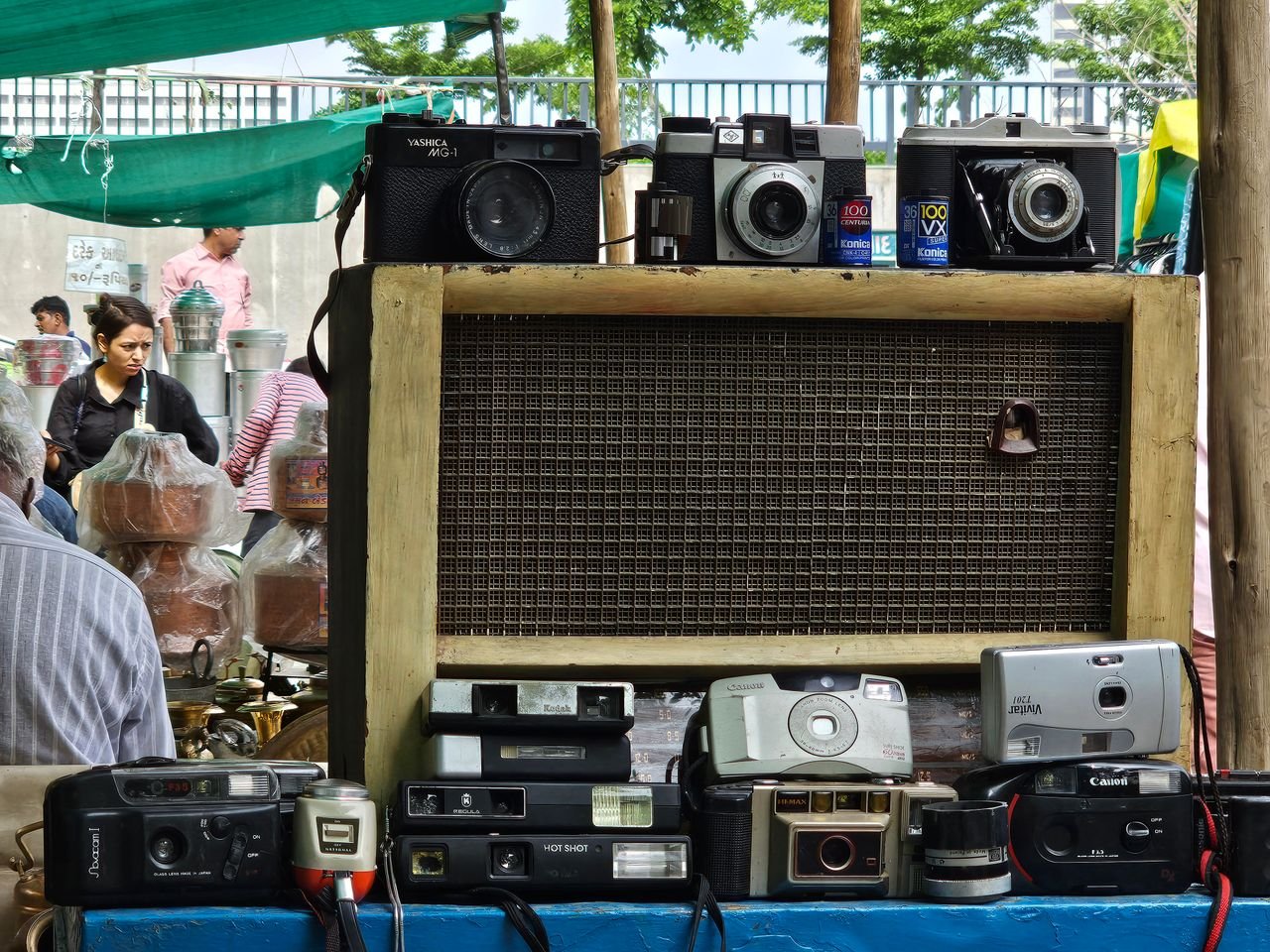Services An assortment of vintage cameras on display at an outdoor market stall with people browsing.