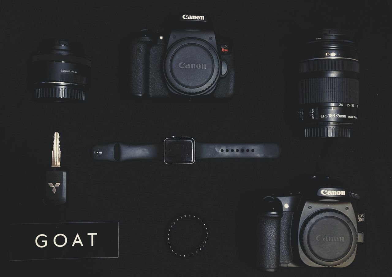 Flat lay of camera gear including Canon, lenses, watch, and key on a dark background.