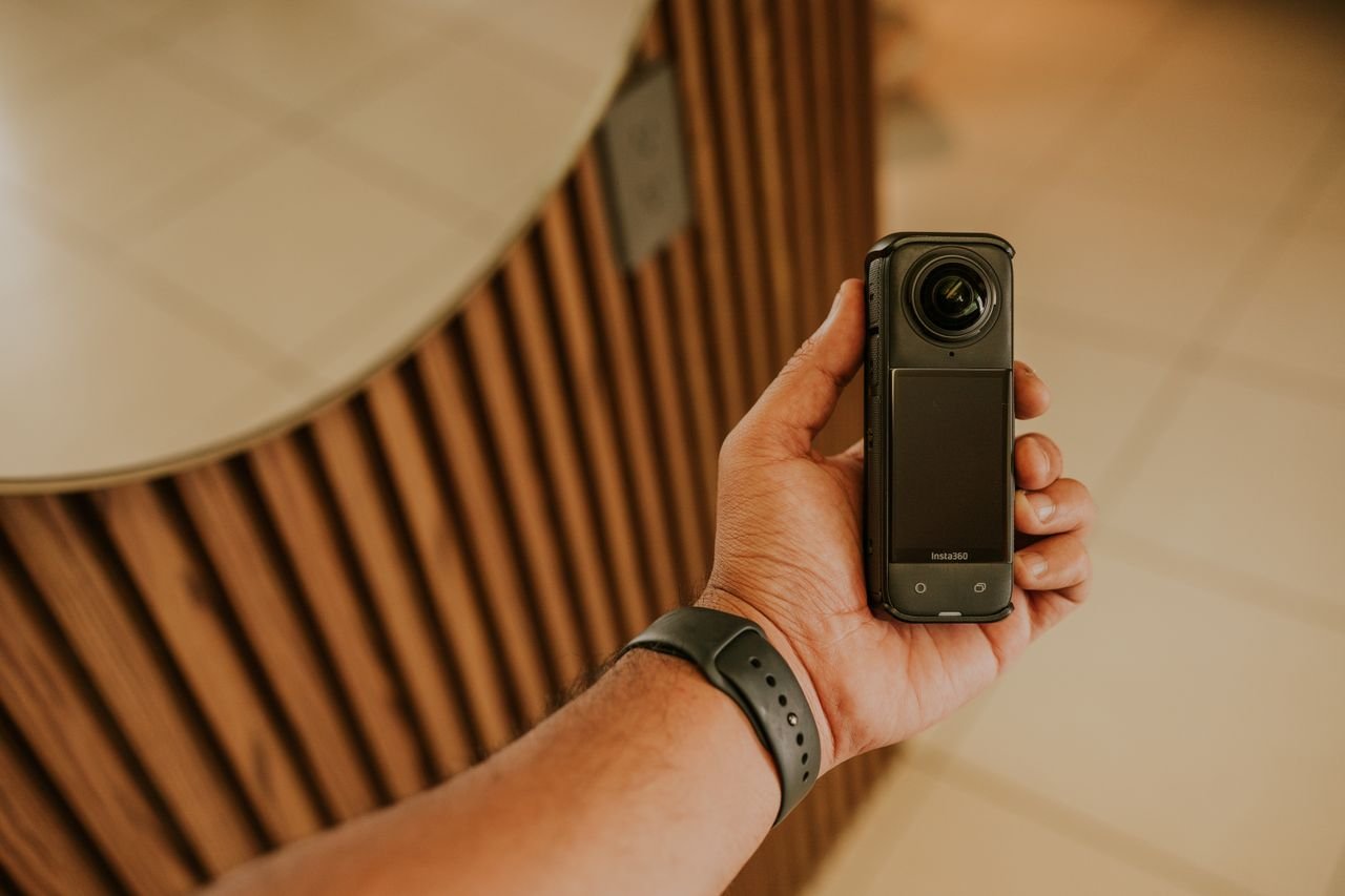 Services Close-up of a hand holding a compact 360-degree camera indoors with modern decor.